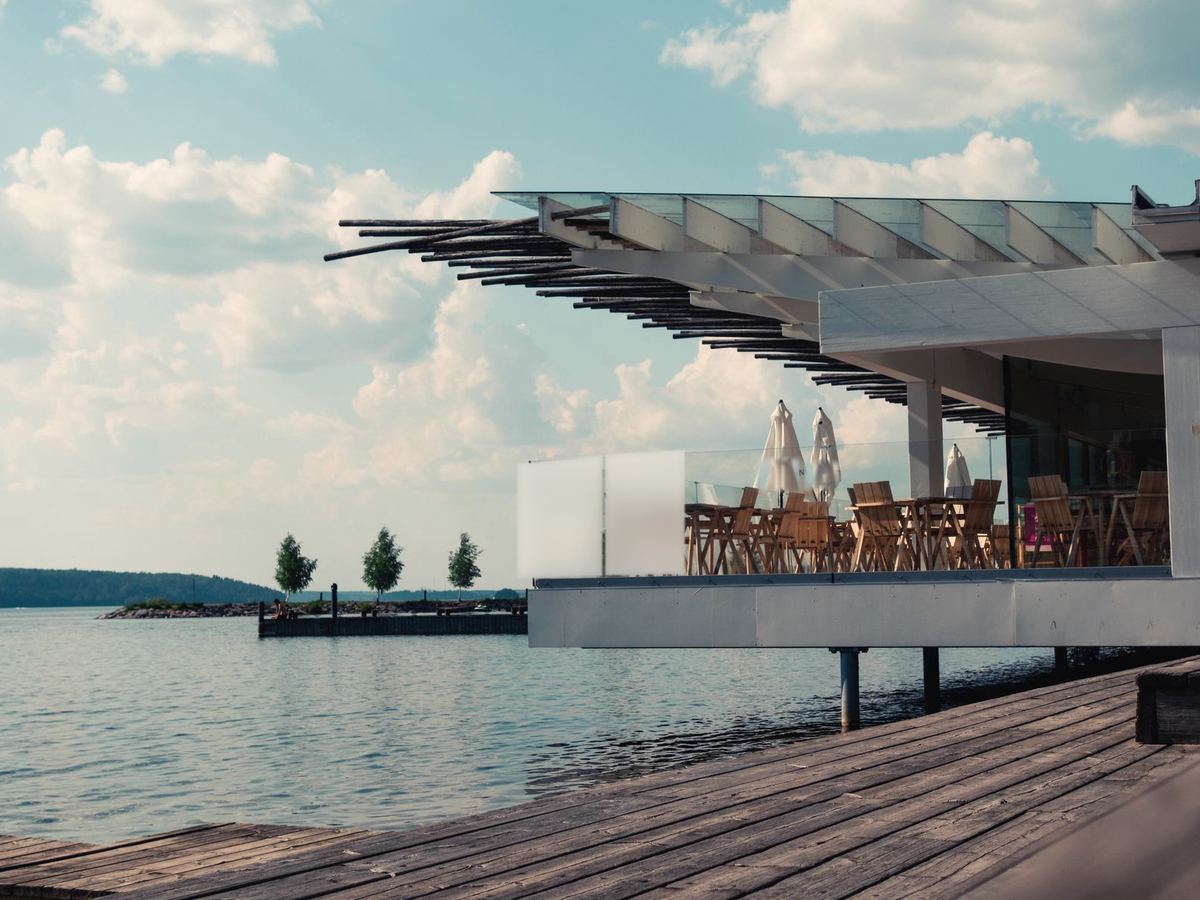 Lakeside deck jutting over the water with switchable glass privacy panels, the frosted section beside clear glass railing against pines and open lake