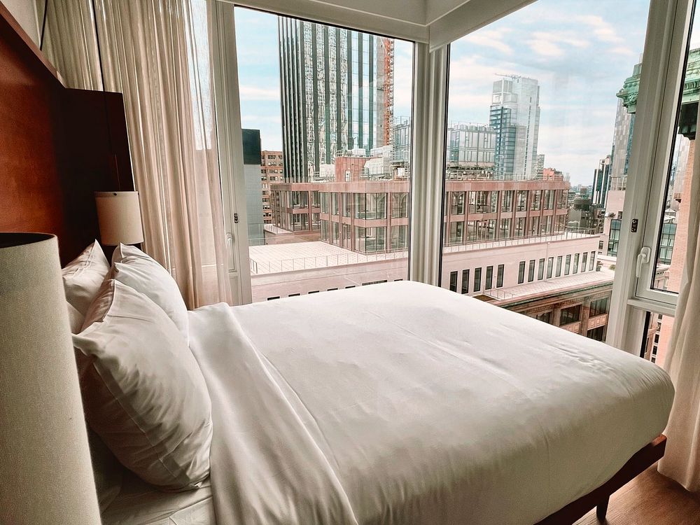 Hotel suite with floor-to-ceiling windows overlooking the city from the bed
