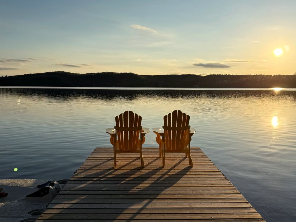 Two Adirondack chairs on a cottage dock at sunset on an Ontario lake