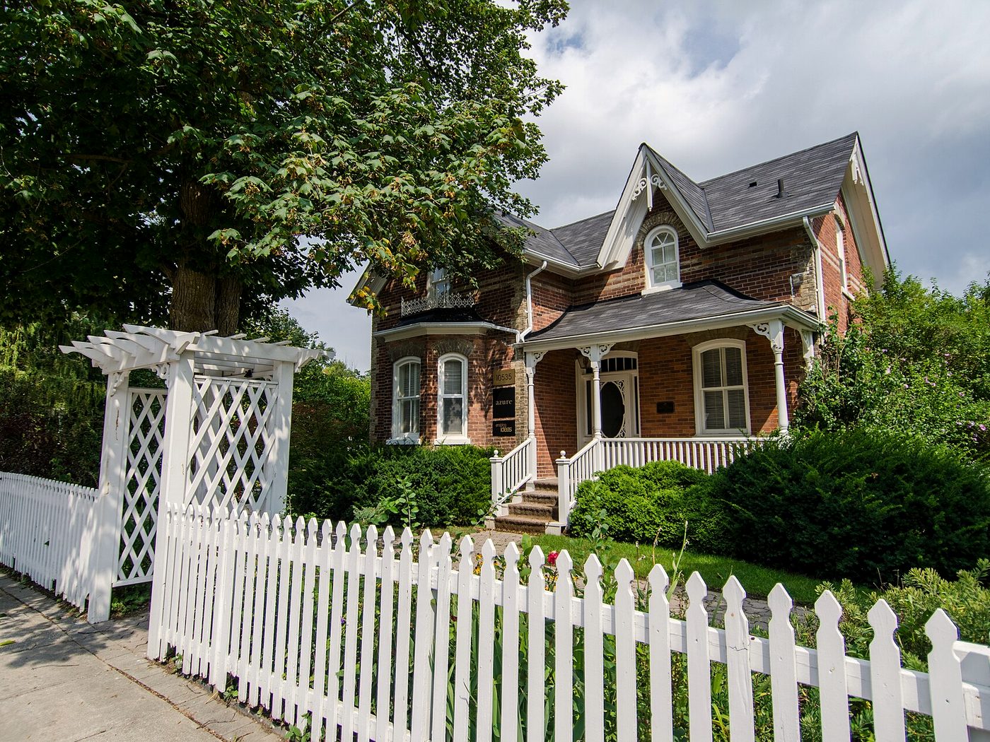 A heritage brick house behind a white picket fence and garden arbour on Islington Avenue in Kleinburg village